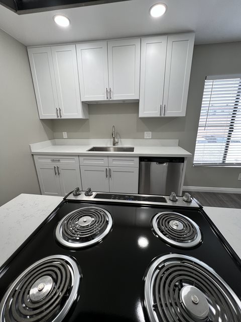 A black stove top in a kitchen with white cabinets.